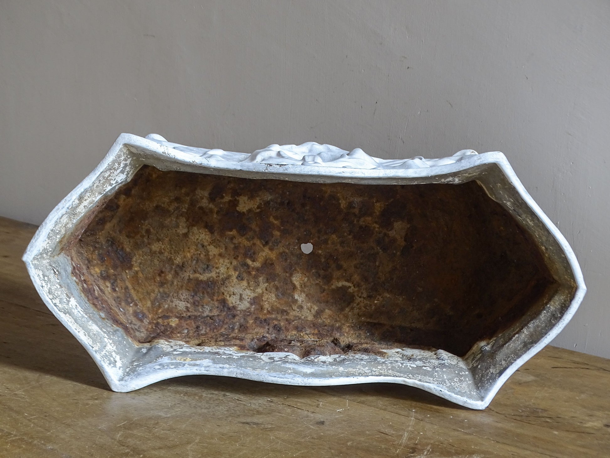 Antique French cast iron jardinière planter with ornate floral relief decoration, scrolling handles and an aged white painted finish.
