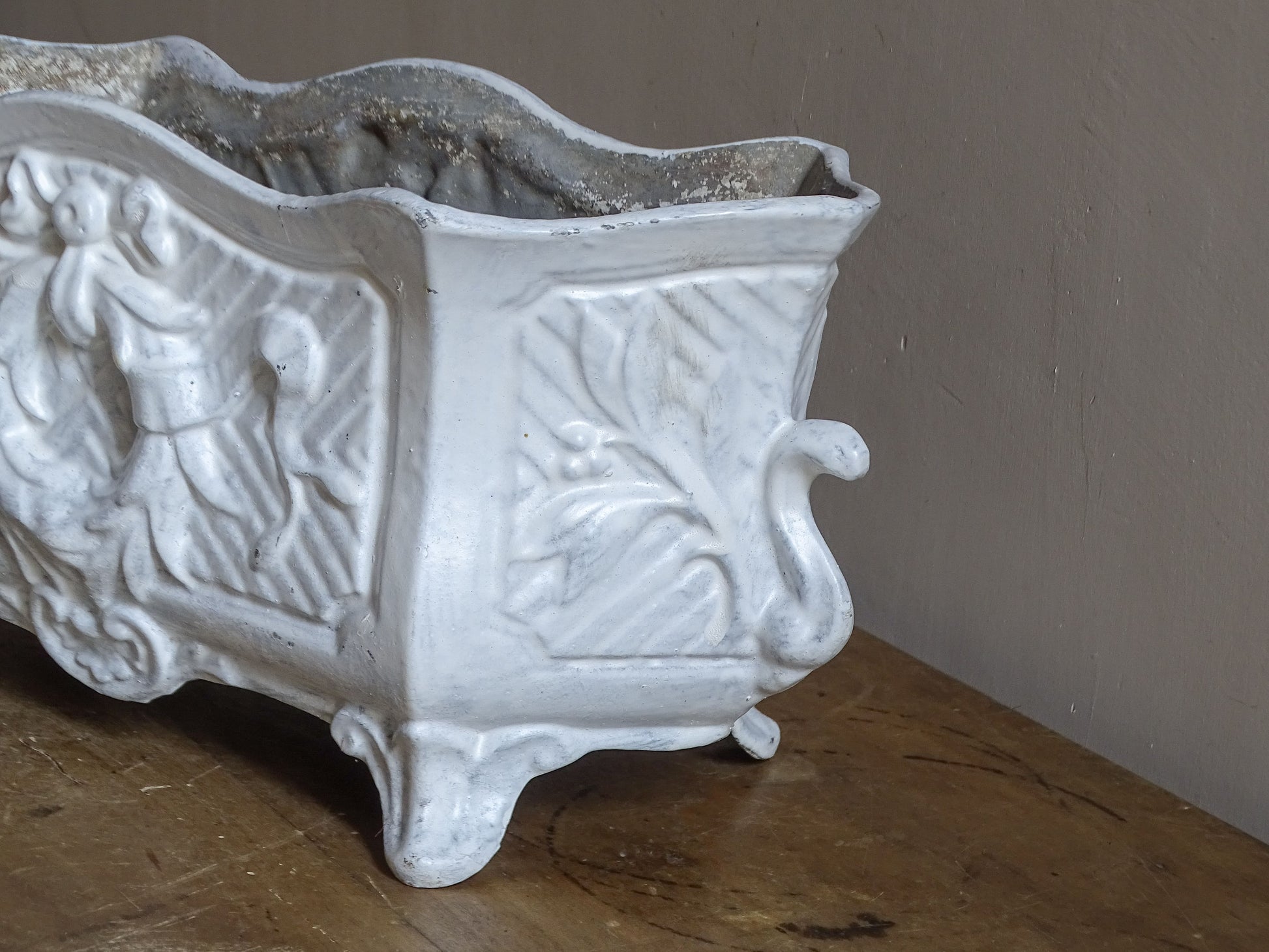 Antique French cast iron jardinière planter with ornate floral relief decoration, scrolling handles and an aged white painted finish.
