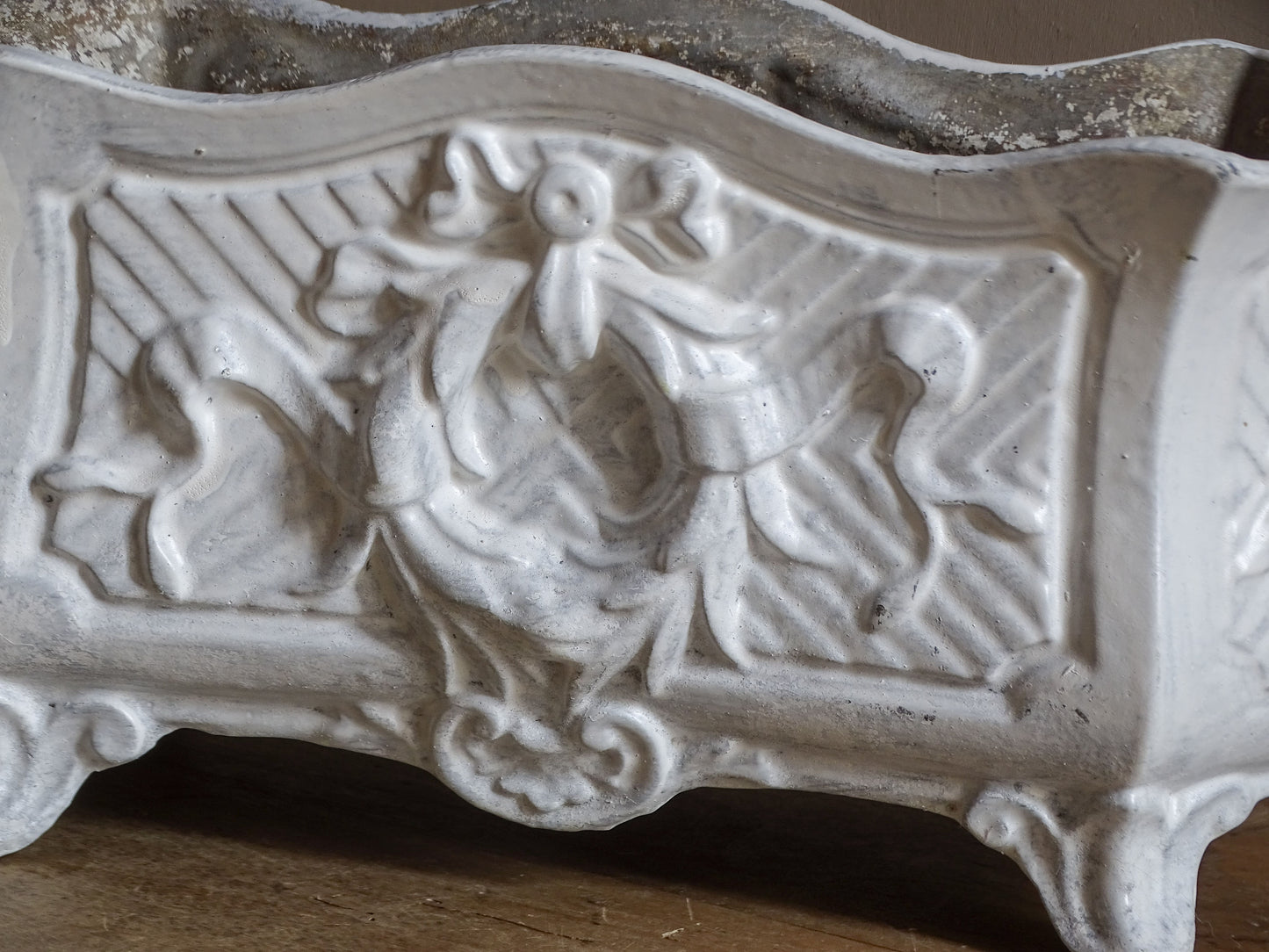 Antique French cast iron jardinière planter with ornate floral relief decoration, scrolling handles and an aged white painted finish.