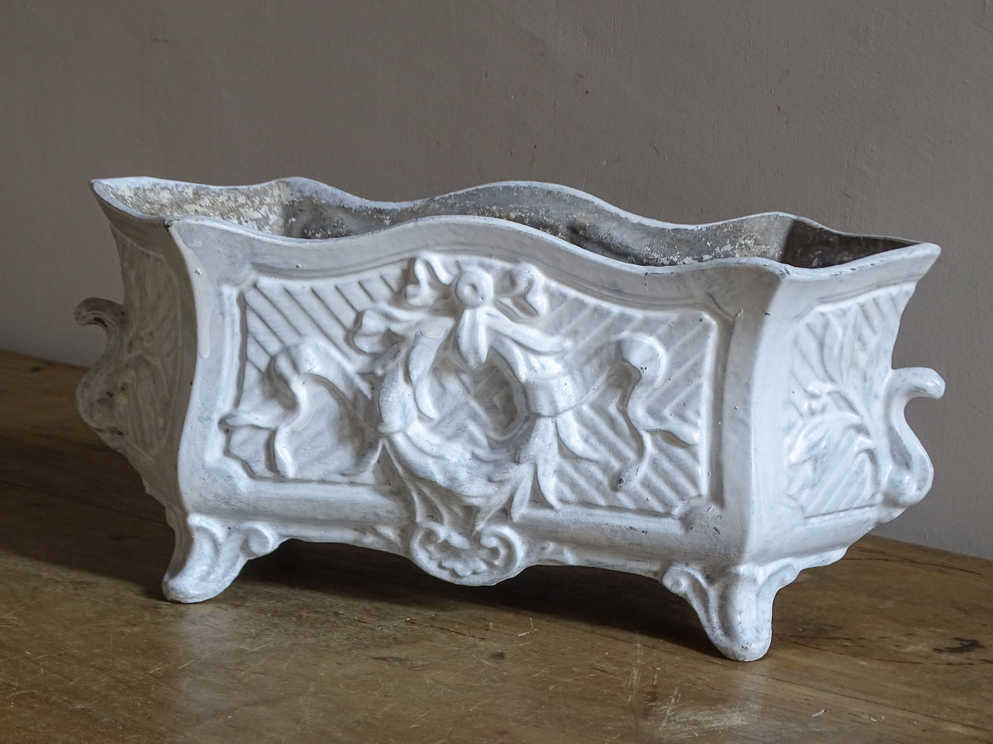 Antique French cast iron jardinière planter with ornate floral relief decoration, scrolling handles and an aged white painted finish.