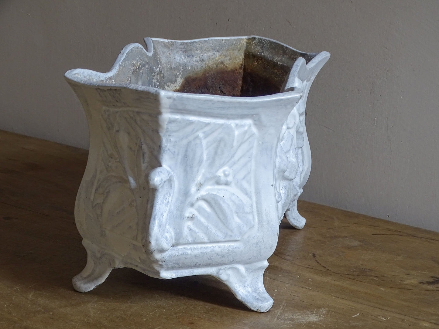Antique French cast iron jardinière planter with ornate floral relief decoration, scrolling handles and an aged white painted finish.