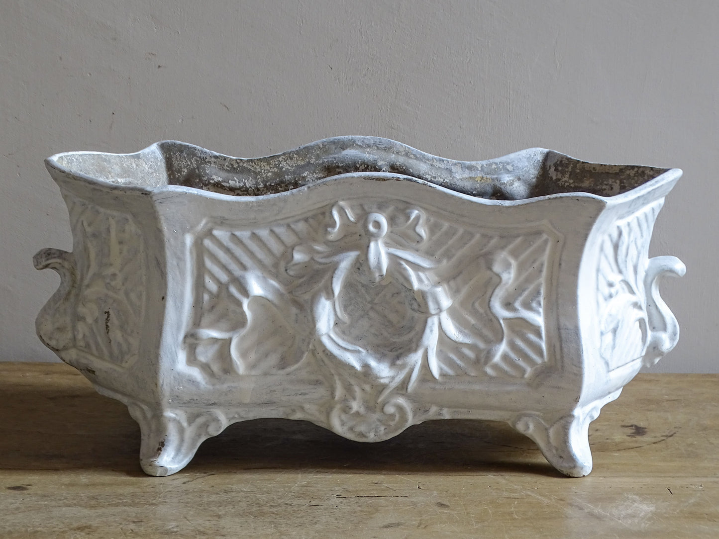 Antique French cast iron jardinière planter with ornate floral relief decoration, scrolling handles and an aged white painted finish.