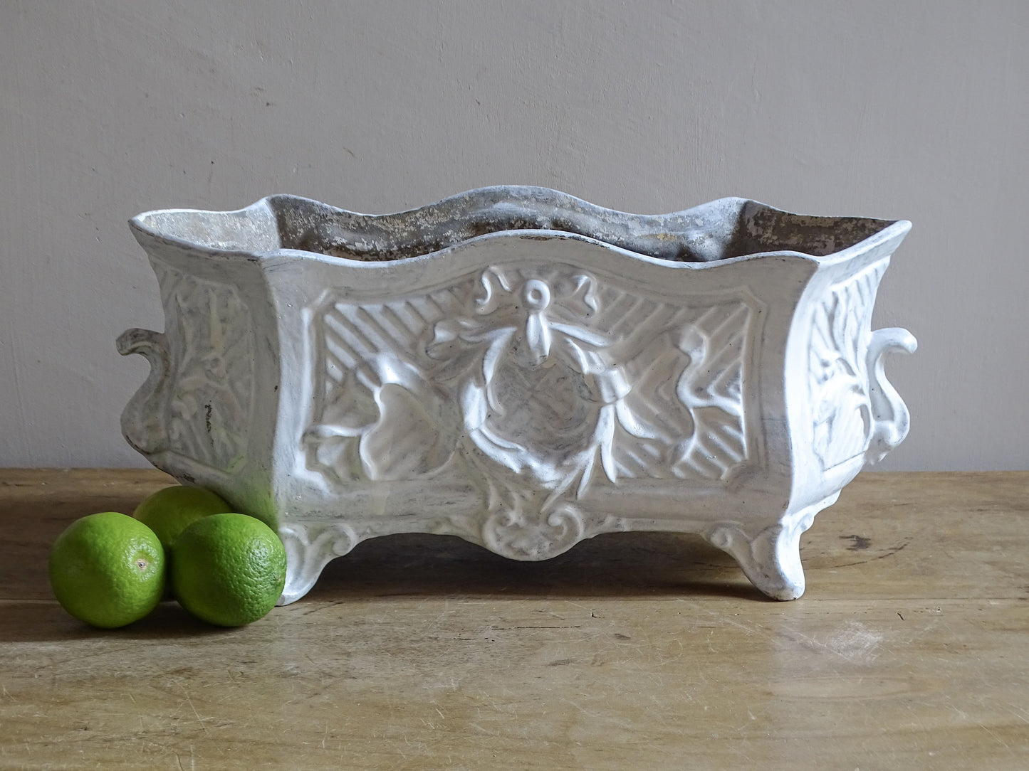 Antique French cast iron jardinière planter with ornate floral relief decoration, scrolling handles and an aged white painted finish.