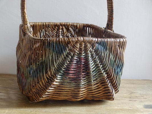 Rear view of a vintage French wicker market basket with red and green painted decoration.