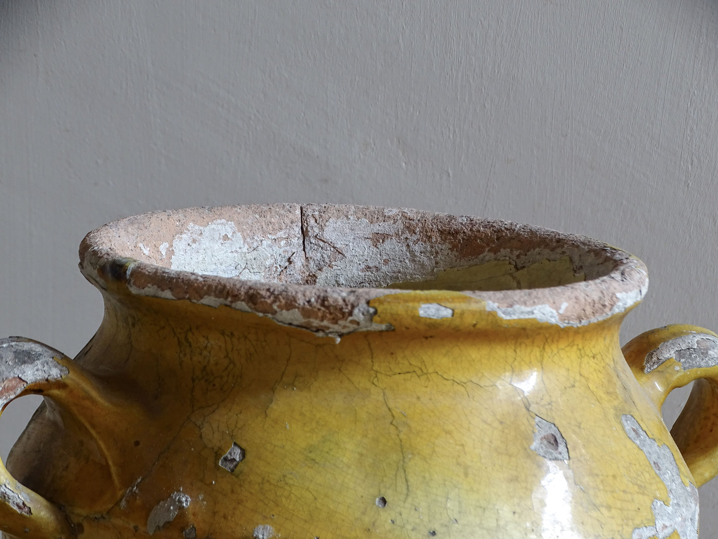 Antique French confit pot with weathered mustard-yellow glaze, twin handles and areas of exposed natural earthenware.