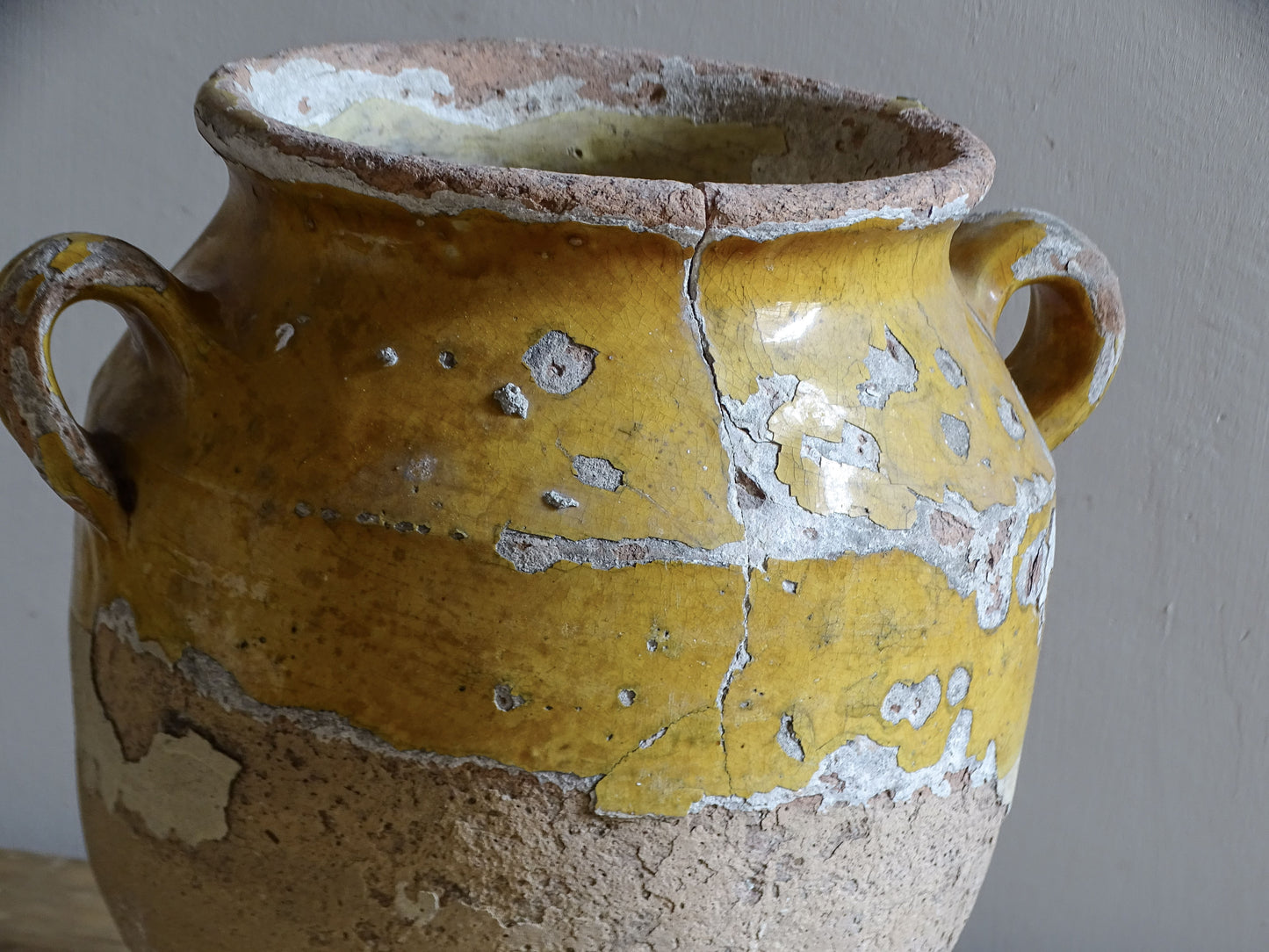 Antique French confit pot with weathered mustard-yellow glaze, twin handles and areas of exposed natural earthenware.