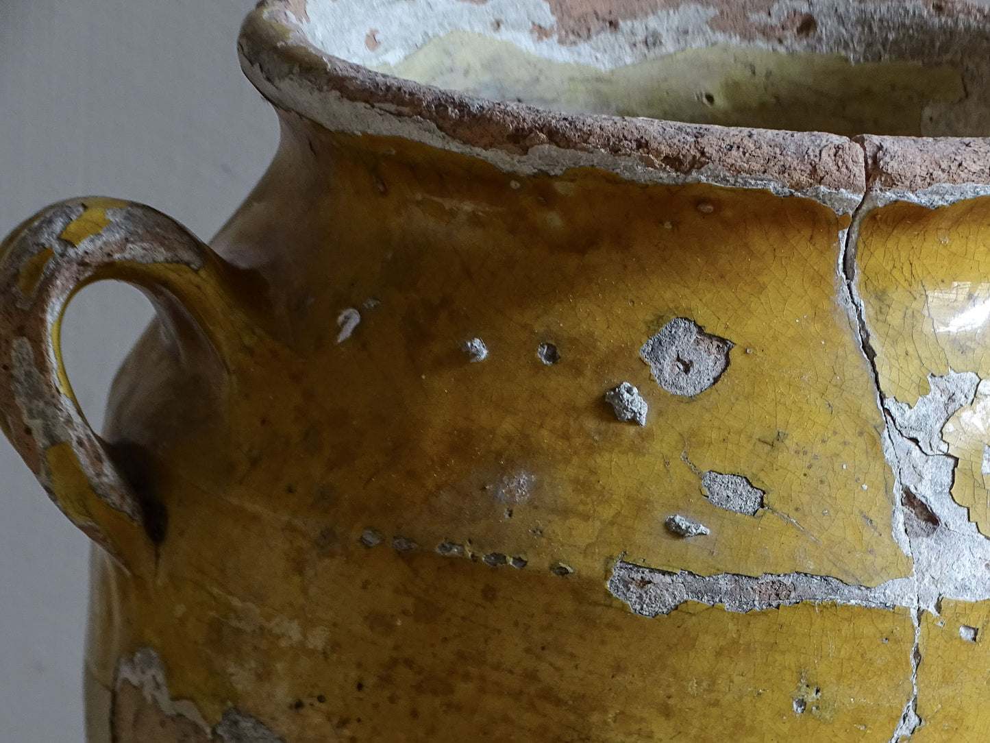 Antique French confit pot with weathered mustard-yellow glaze, twin handles and areas of exposed natural earthenware.
