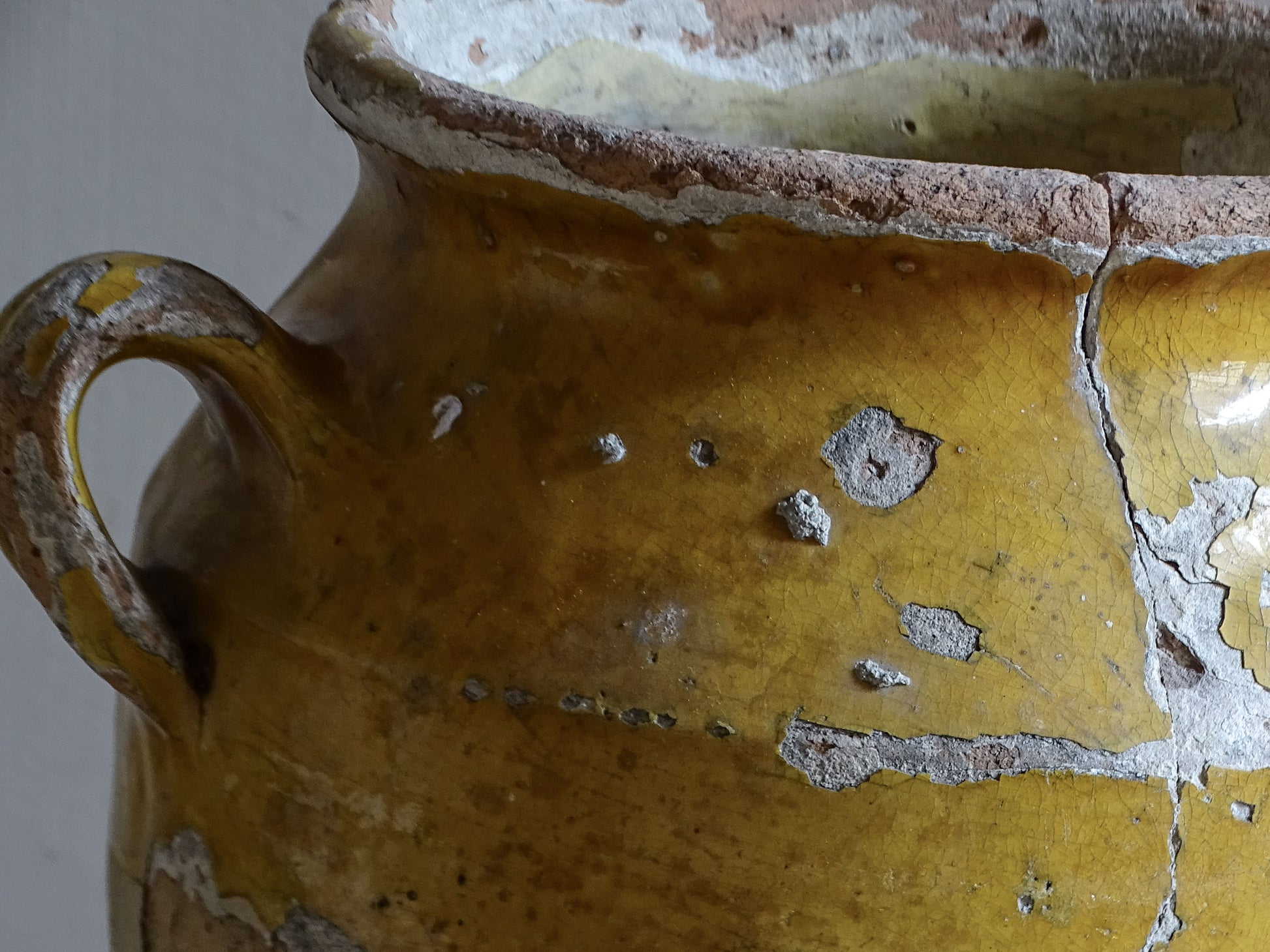 Antique French confit pot with weathered mustard-yellow glaze, twin handles and areas of exposed natural earthenware.