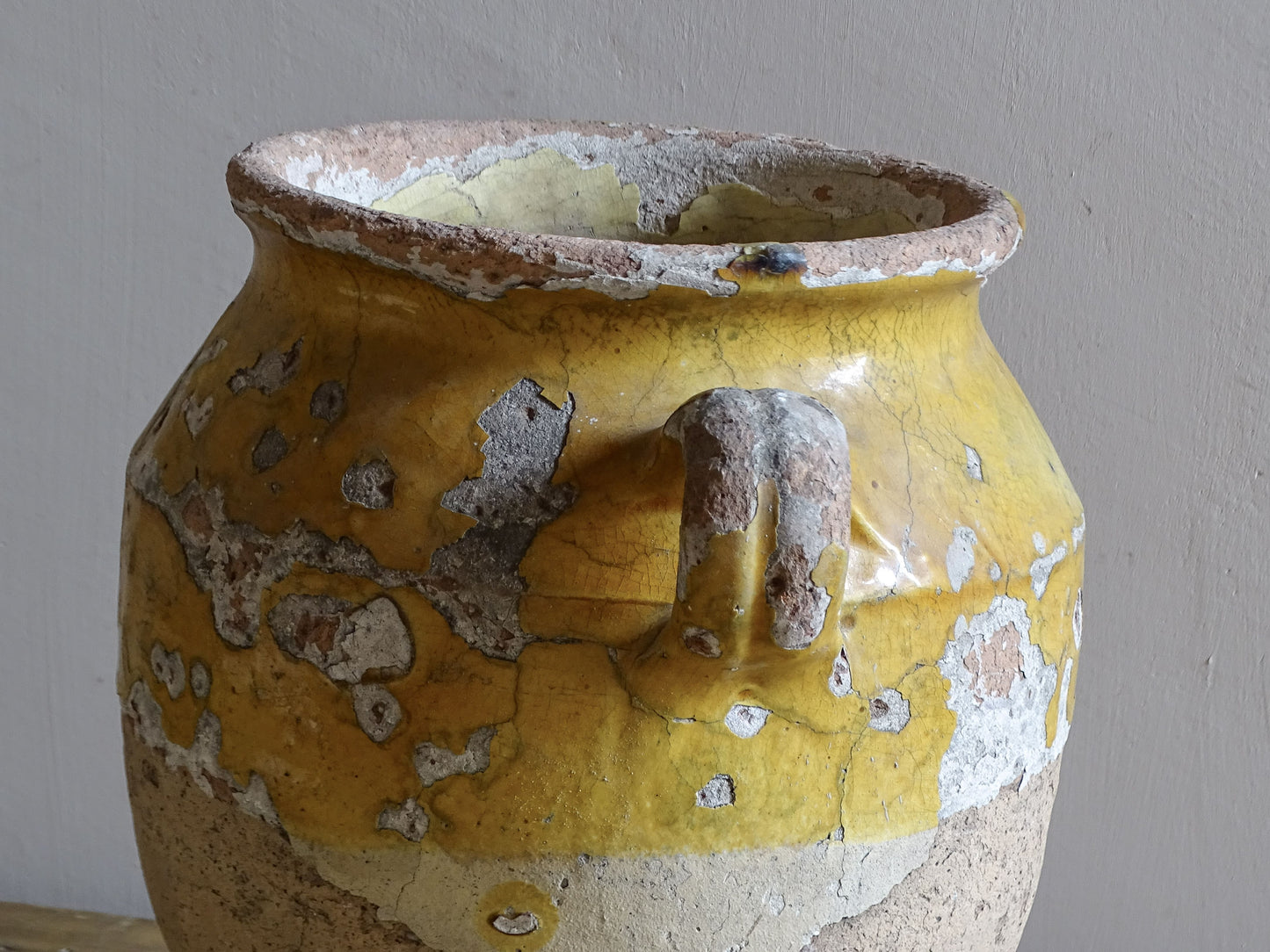 Antique French confit pot with weathered mustard-yellow glaze, twin handles and areas of exposed natural earthenware.