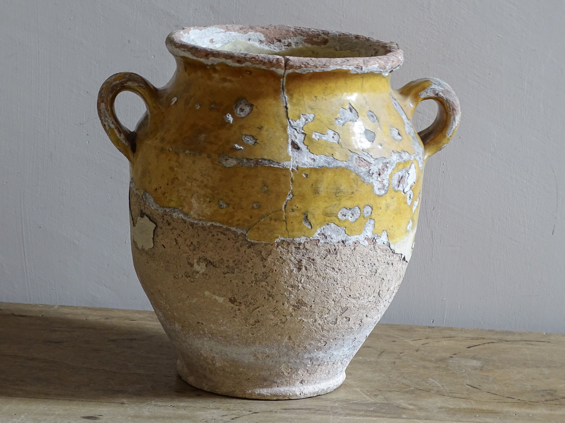 Antique French confit pot with weathered mustard-yellow glaze, twin handles and areas of exposed natural earthenware.