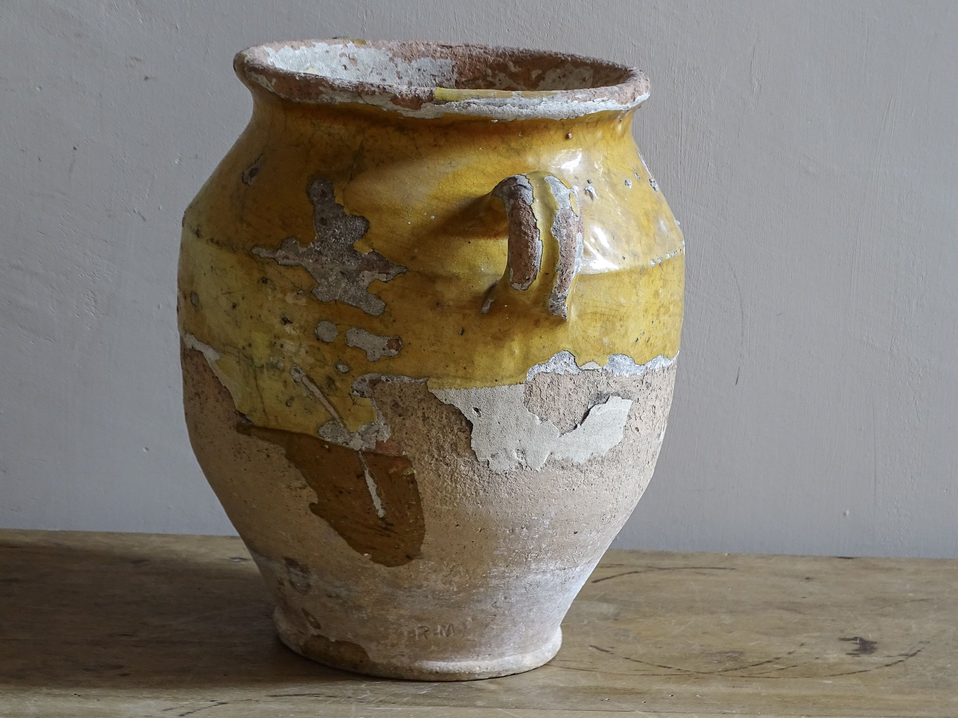 Antique French confit pot with weathered mustard-yellow glaze, twin handles and areas of exposed natural earthenware.