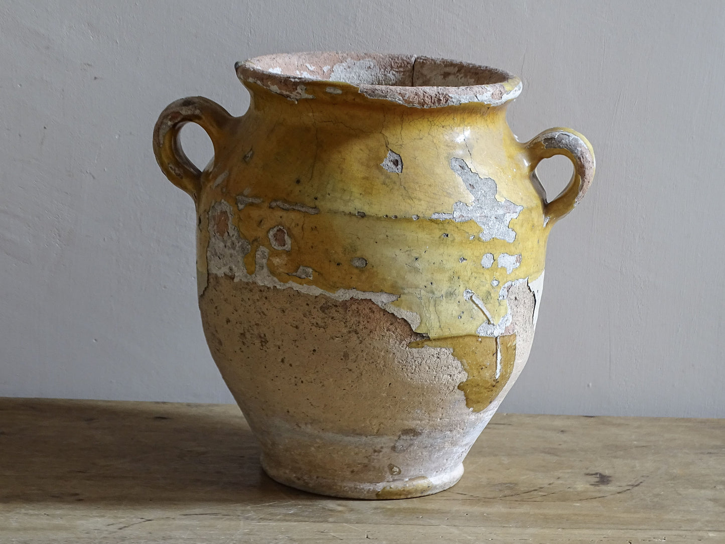 Antique French confit pot with weathered mustard-yellow glaze, twin handles and areas of exposed natural earthenware.