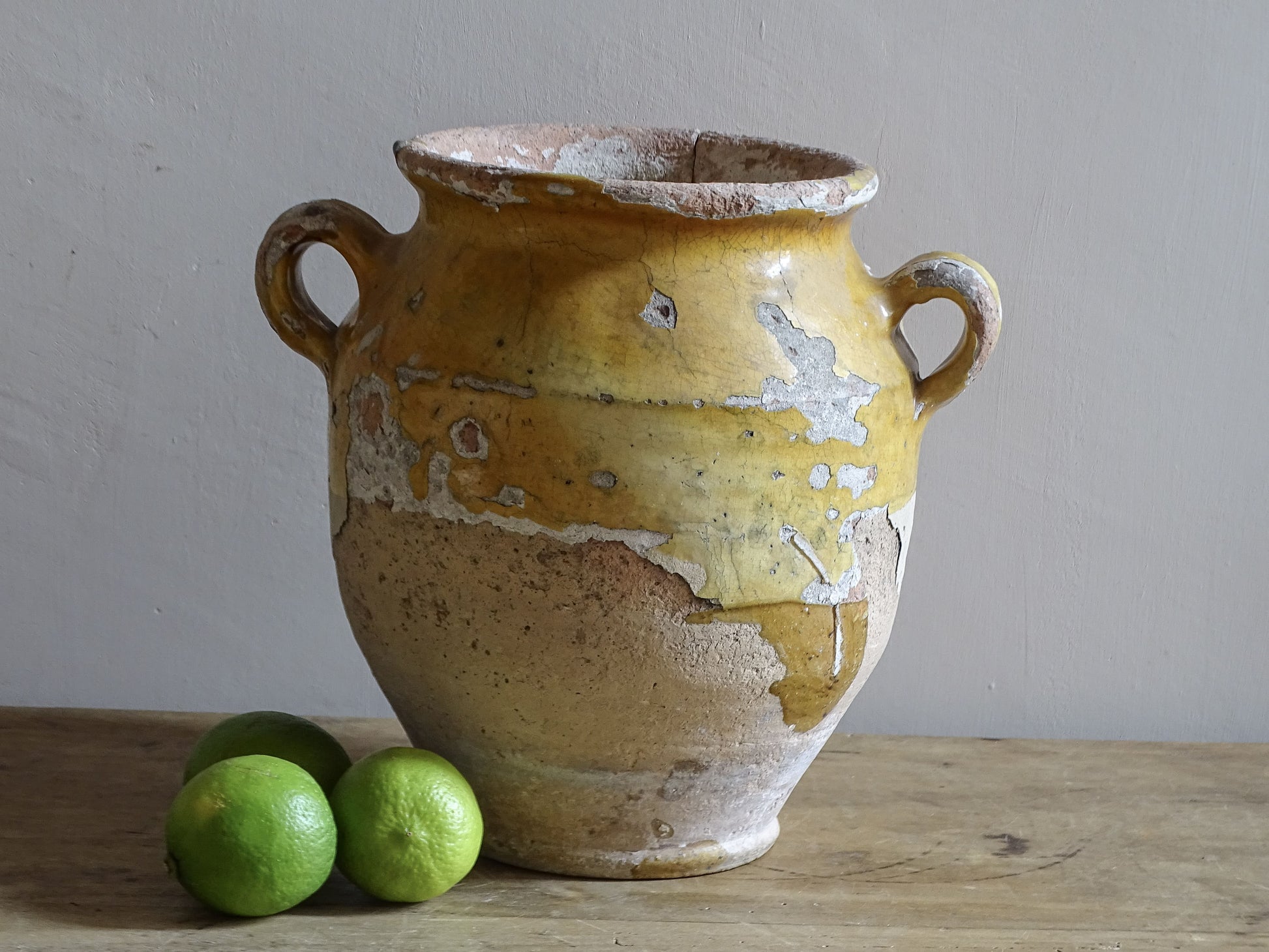 Antique French confit pot with weathered mustard-yellow glaze, twin handles and areas of exposed natural earthenware.