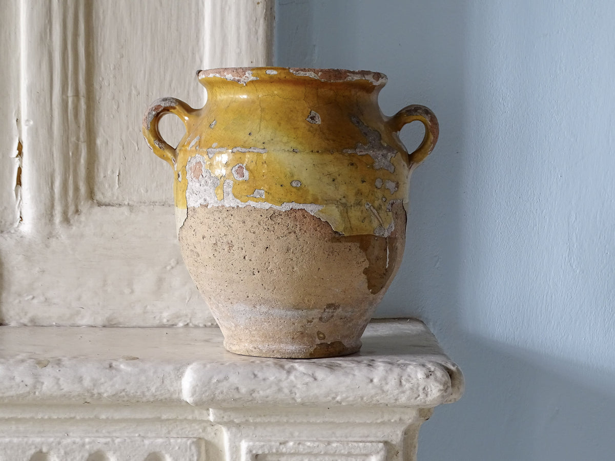 Antique French confit pot with yellow glaze displayed on a country house fireplace