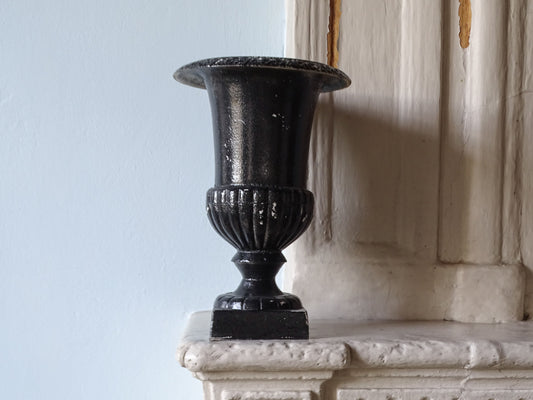 French antique cast iron urn in black on a country house fireplace next to pale blue painted wall