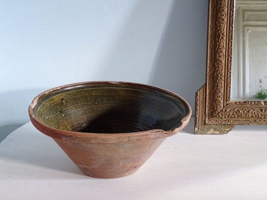 French antique ceramic bowl with a dark green glaze, pictured next to a gold mirror in front of a pale blue wall