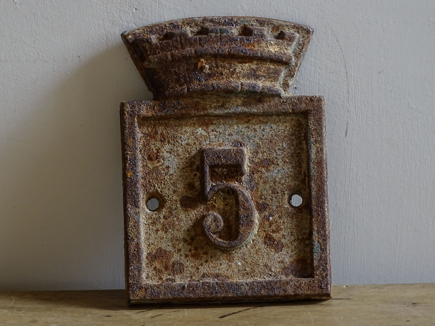 Close view of a weathered French cast iron house number plaque No. 5 with raised border and decorative fortified crest.