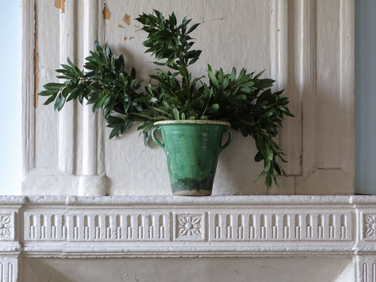 French country garden planter in green glazed antique earthenware displayed on a fireplace filled with greenery