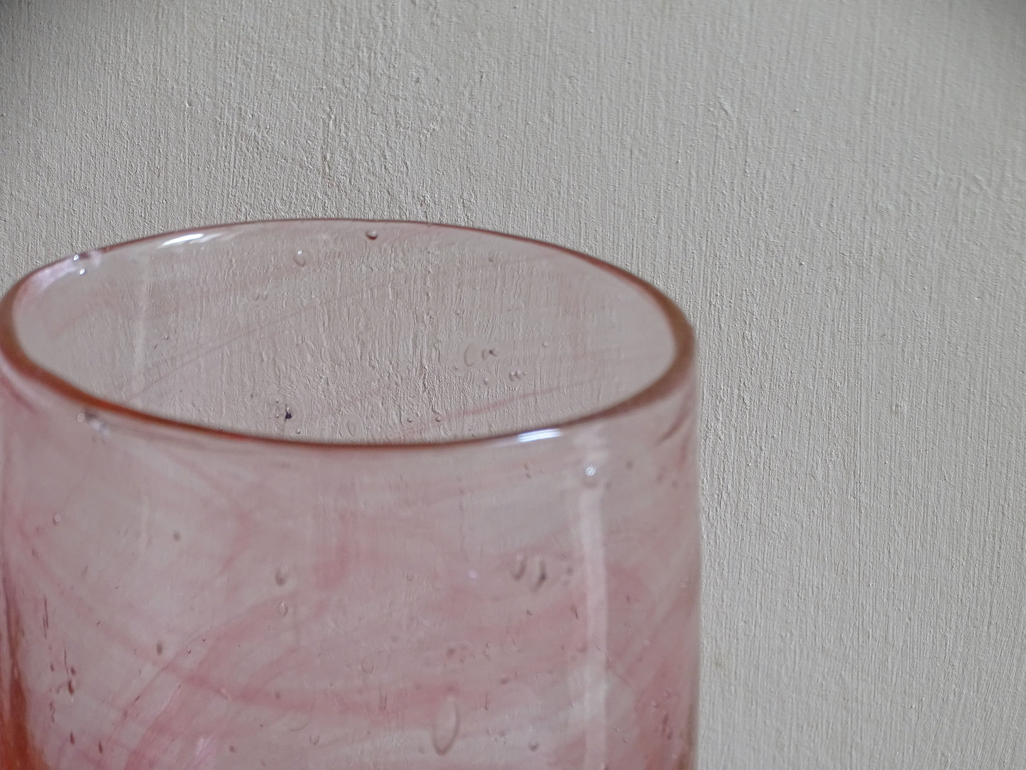 Pale pink hand-blown glass tumbler with deeper rose swirls and bubbles