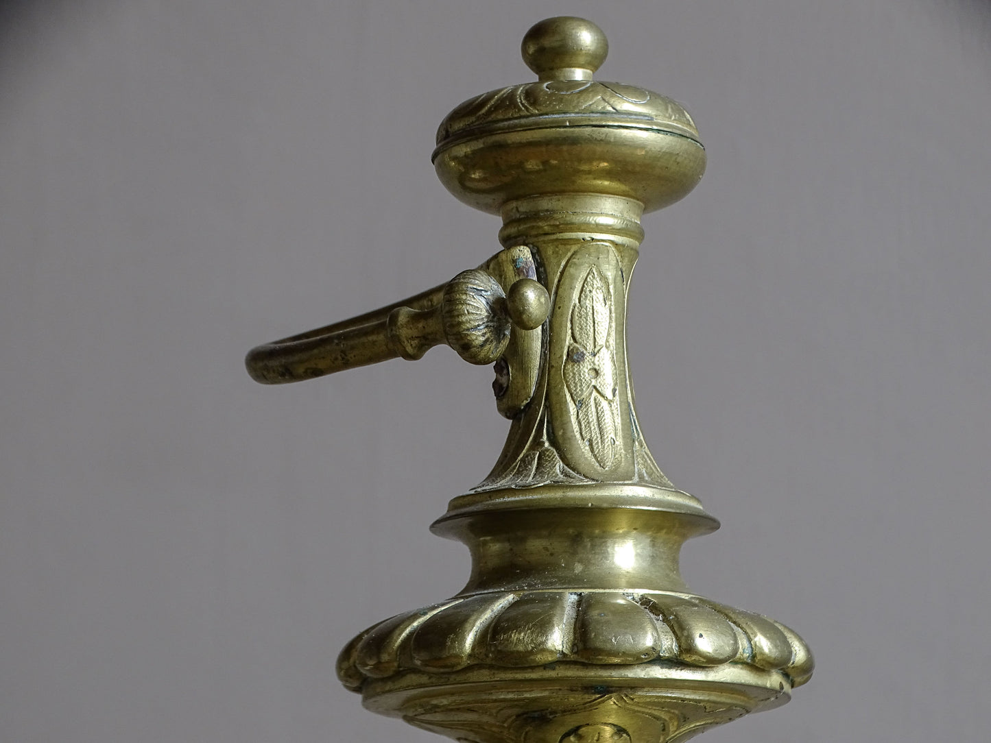 Detail of aged brass French chenet with classical female mascaron and scroll decoration