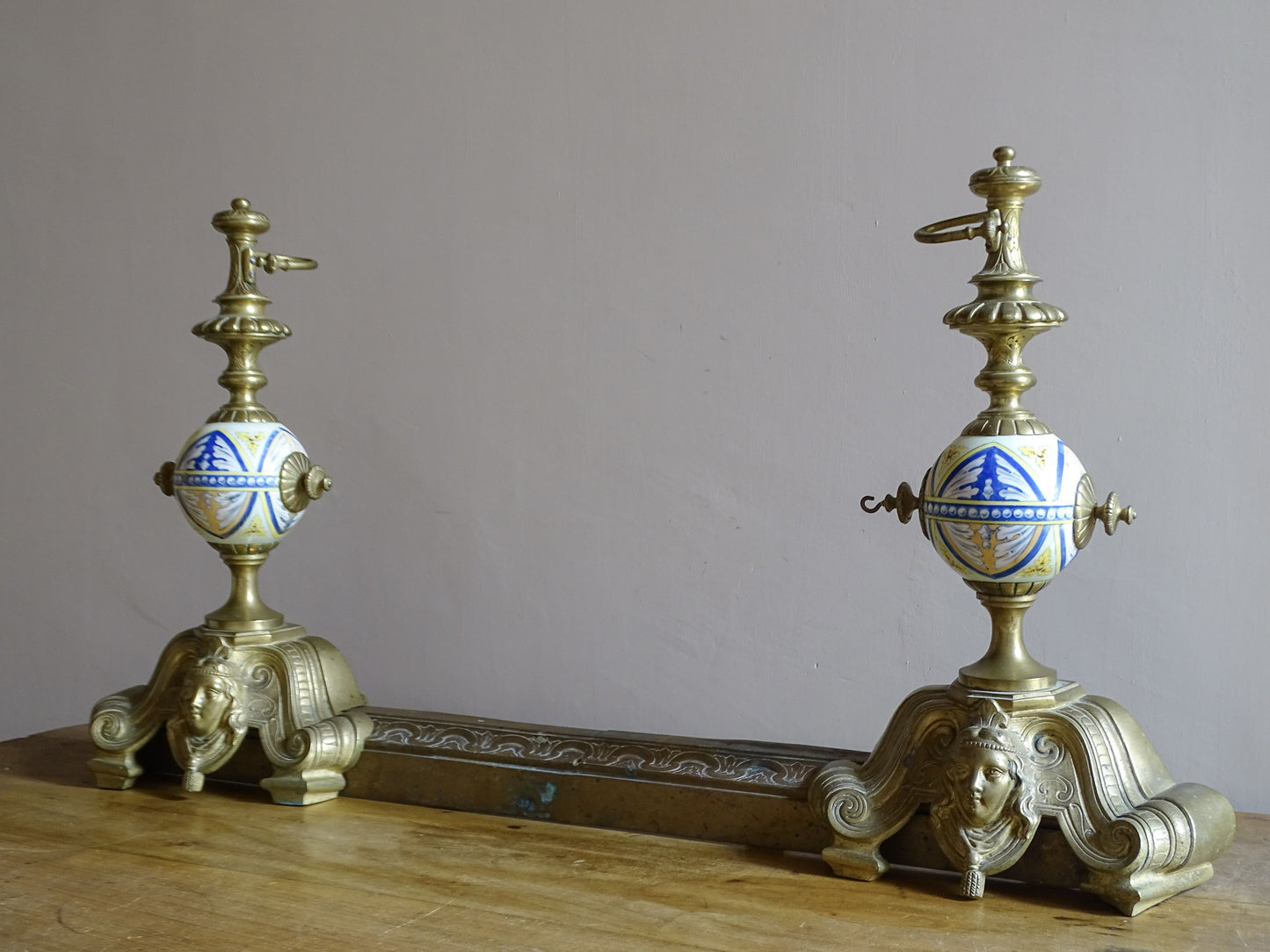 Antique French brass fireplace chenets with hand-painted polychrome ceramic globes, female mascaron decoration and matching sliding fender
