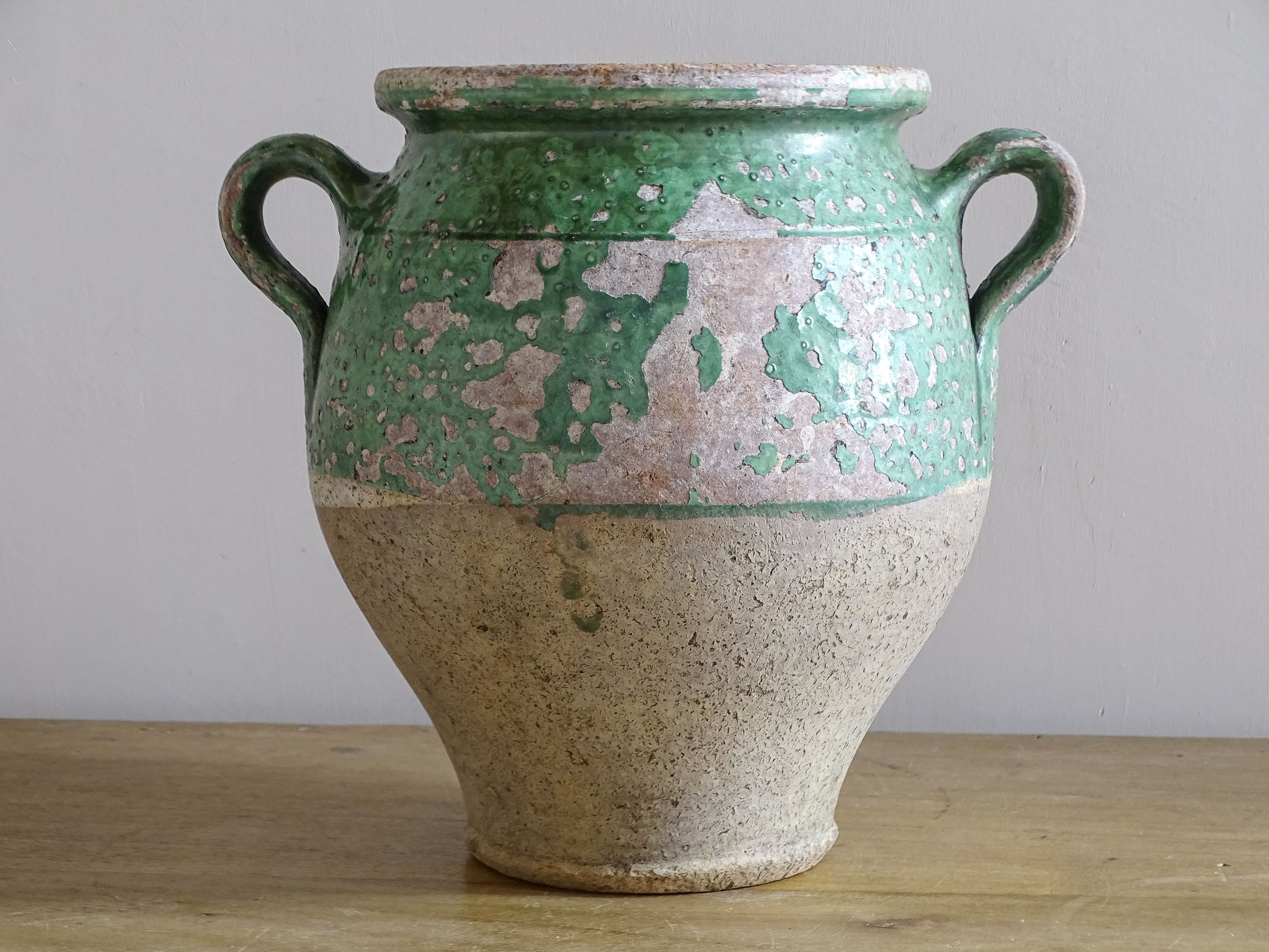 Side view of antique green glazed confit pot with loop handle