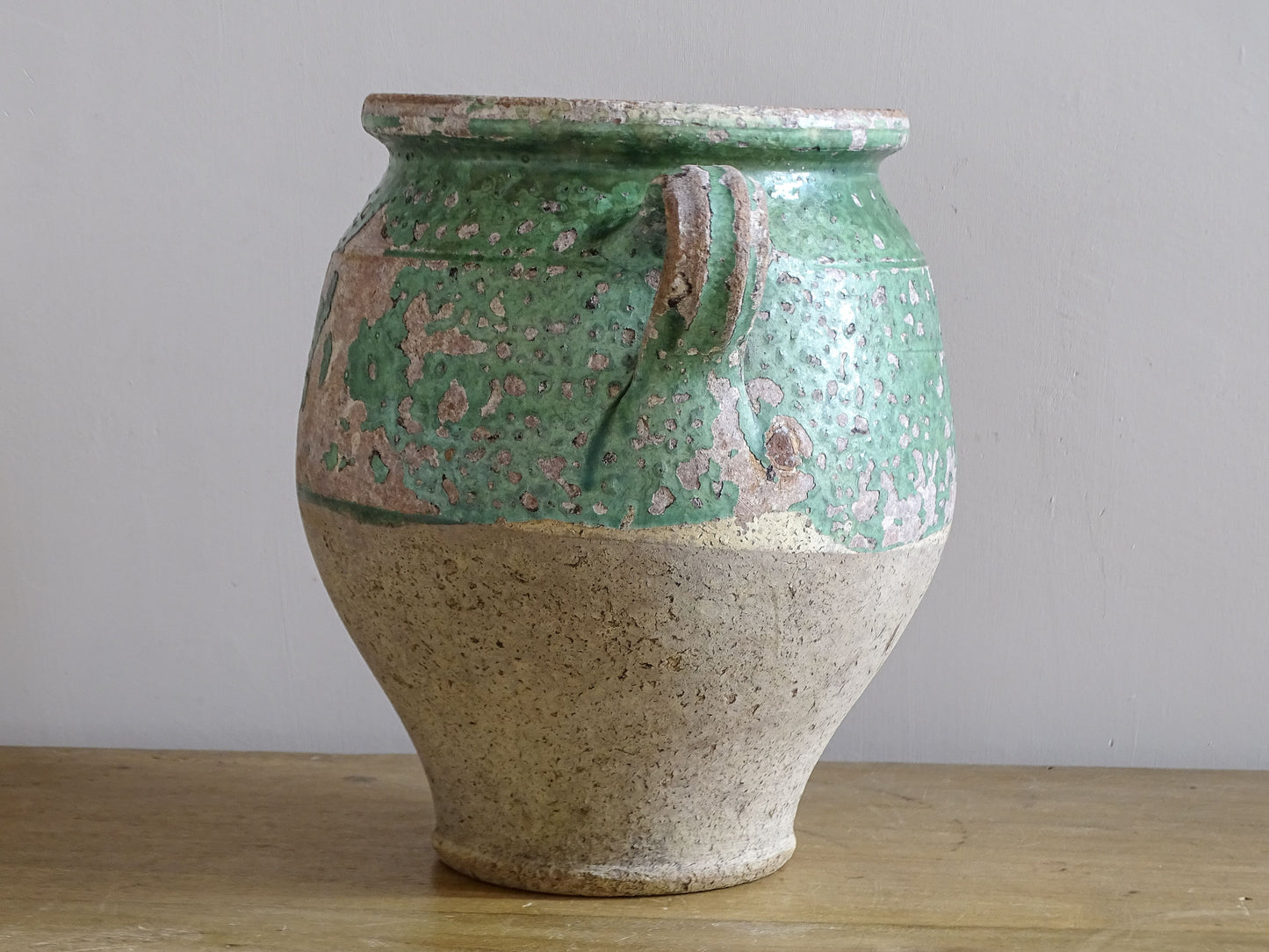 Side view of antique green glazed confit pot with loop handle