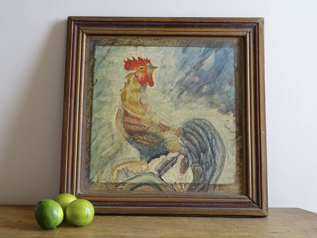 Framed French rooster oil painting displayed on a table with fresh green limes