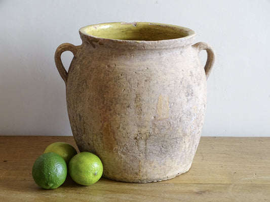 Antique French confit pot with weathered terracotta exterior, two handles and yellow glazed interior