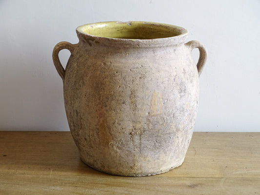 Antique French confit pot with weathered terracotta exterior, two handles and yellow glazed interior