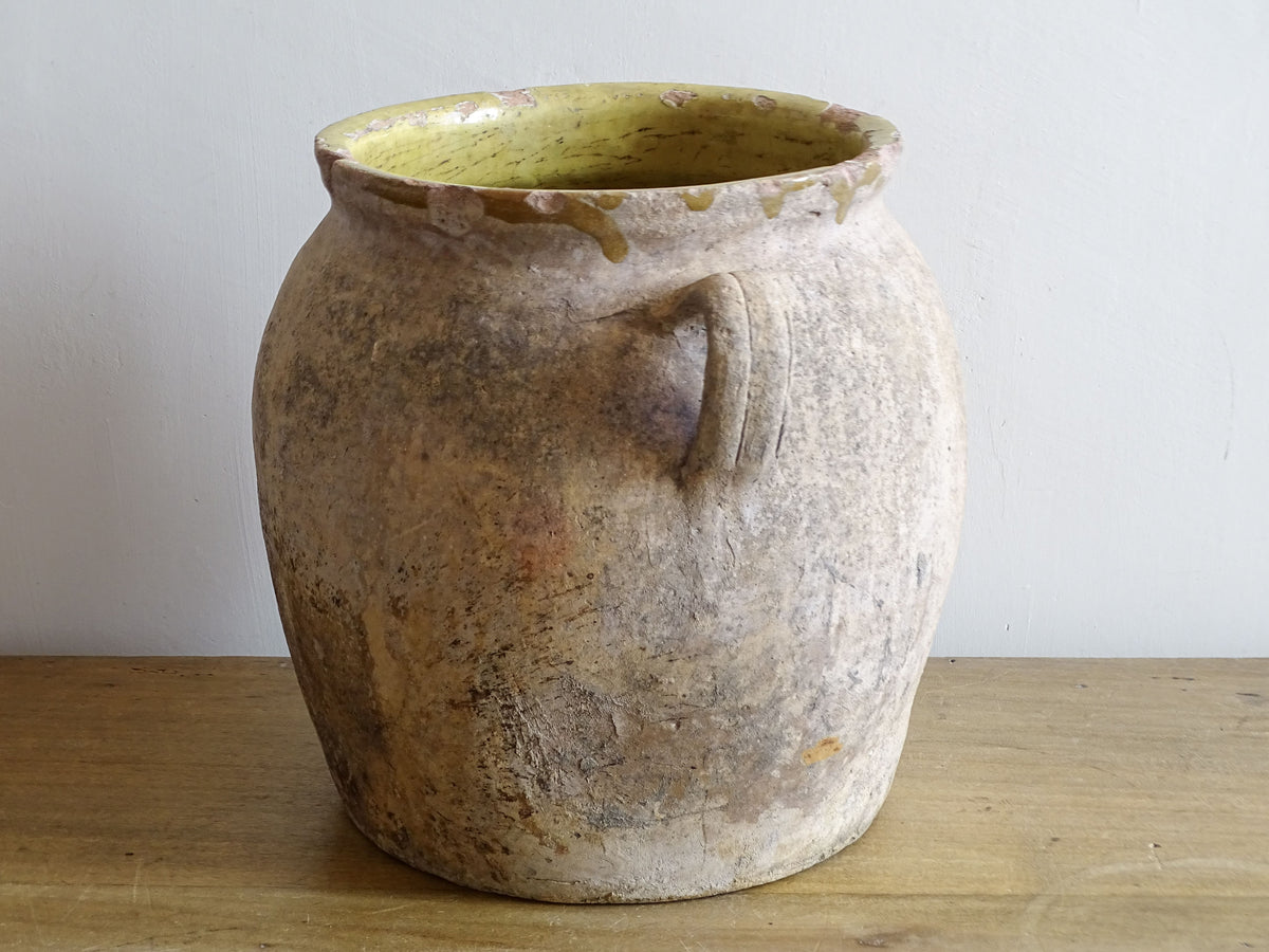 Side view of antique French confit pot with worn terracotta surface and yellow glazed rim