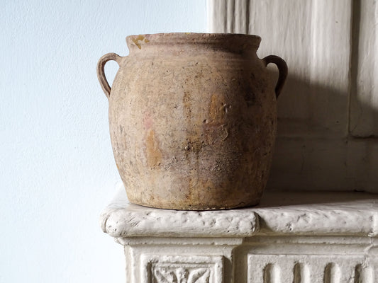Antique French confit pot with weathered terracotta exterior, two handles and yellow glazed interior, pictured on a country house fireplace