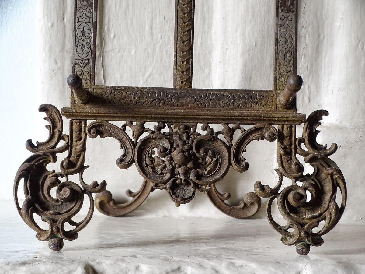 Detailed view of the decorative cast iron base of an antique tabletop easel, featuring floral motifs and scrolling ornamentation