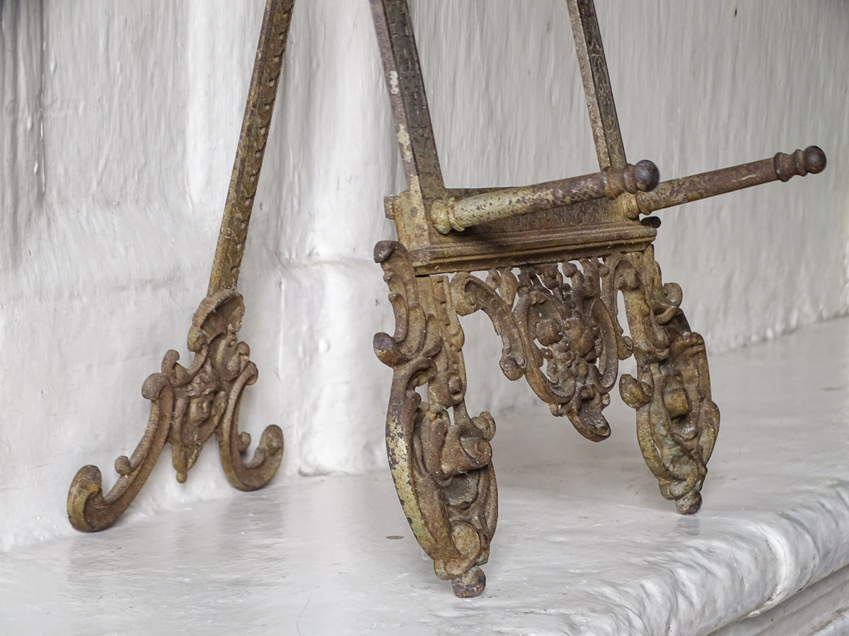 Side detail of an antique German cast iron tabletop easel showing its ornate feet, decorative supports and aged surface