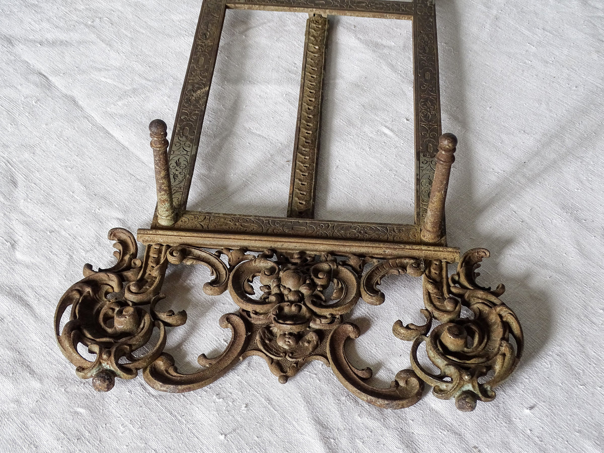 Detailed view of the decorative cast iron base of an antique tabletop easel, featuring floral motifs and scrolling ornamentation