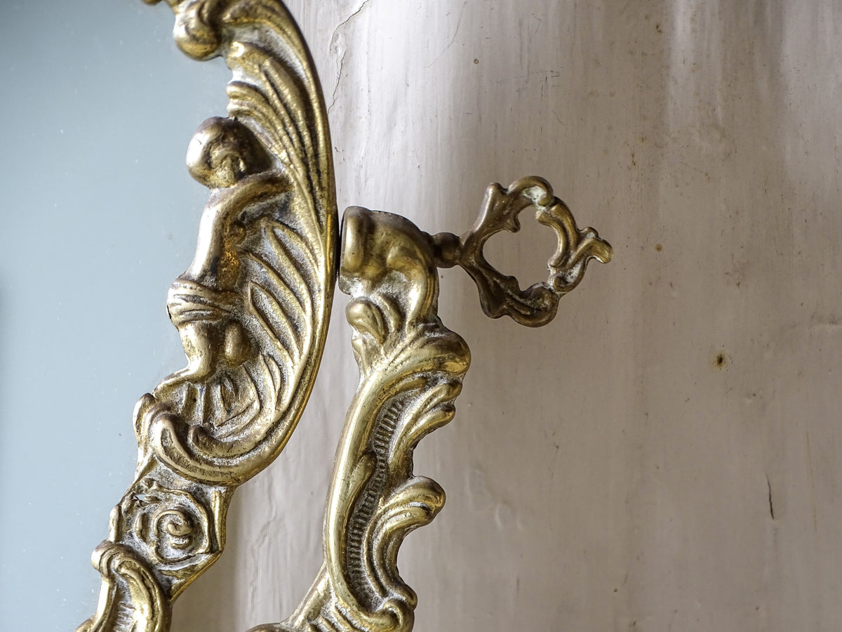 Close-up of a cherub figure and functional adjustment screw on a vintage brass tilting vanity mirror.