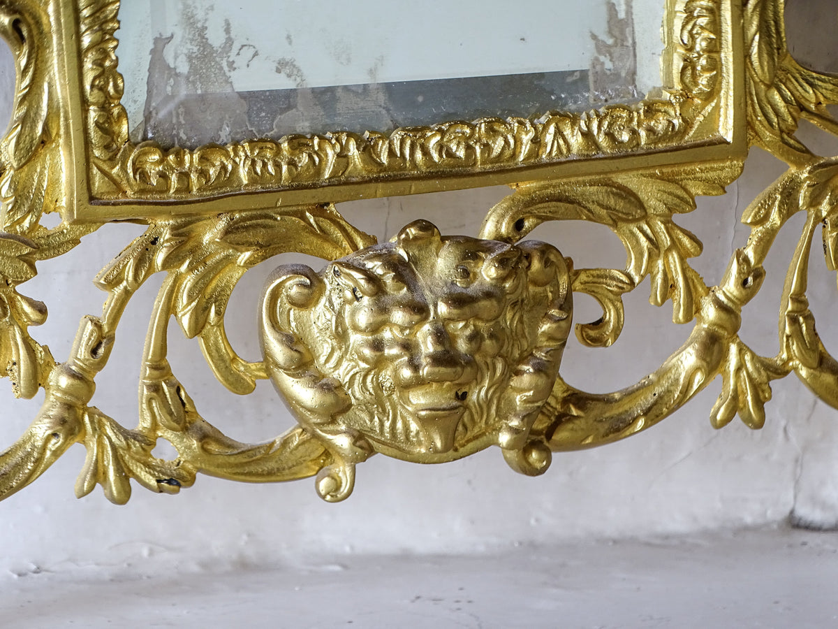 Lower section of the gilt metal mirror showing the aged bevelled glass, elaborate foliage and grotesque mask