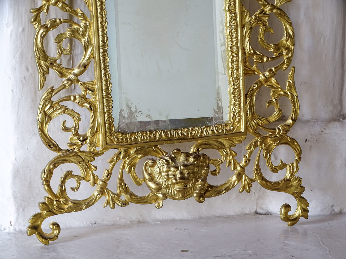 Close-up of the grotesque mask and decorative gilt metal scrollwork beneath the antique French mirror