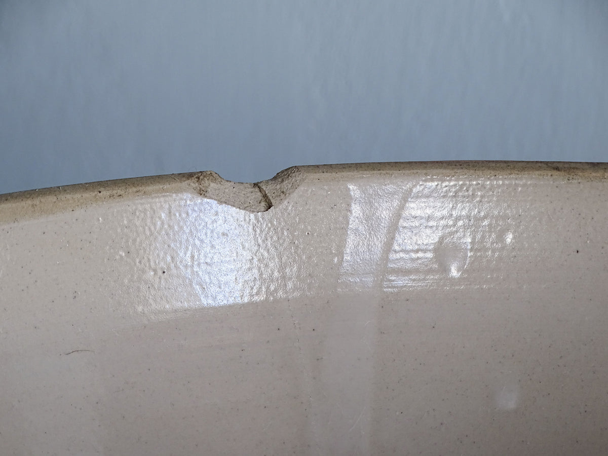 Close-up showing a chip to the rim of a vintage French stoneware mixing bowl.