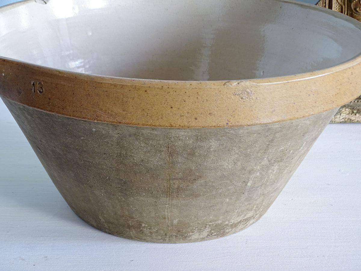 Side view of a large French vintage stoneware mixing bowl with a cream interior and unglazed grey exterior.
