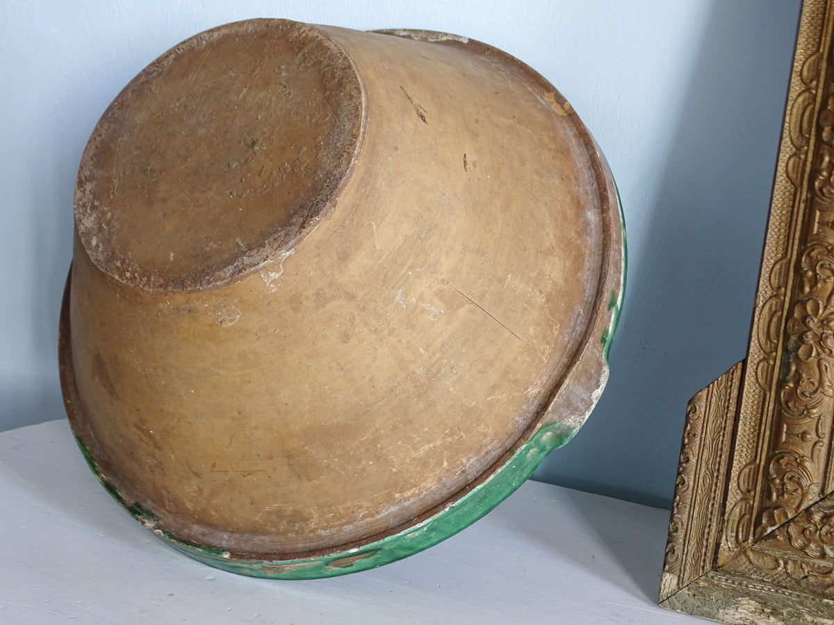 Underside of a large antique French tian bowl showing its unglazed terracotta exterior and green glazed rim.