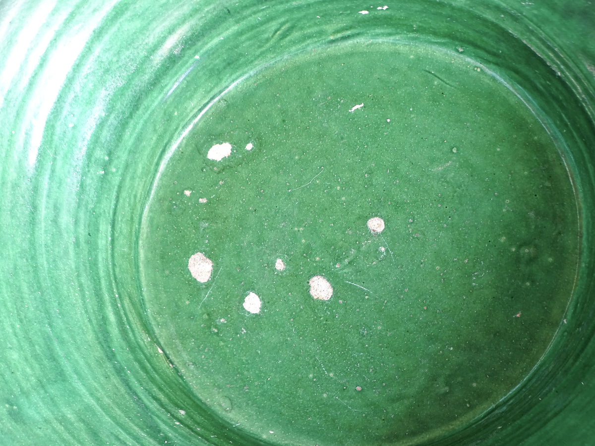 Close-up of the rich green glazed interior of an antique French tian bowl, showing small areas of glaze loss.