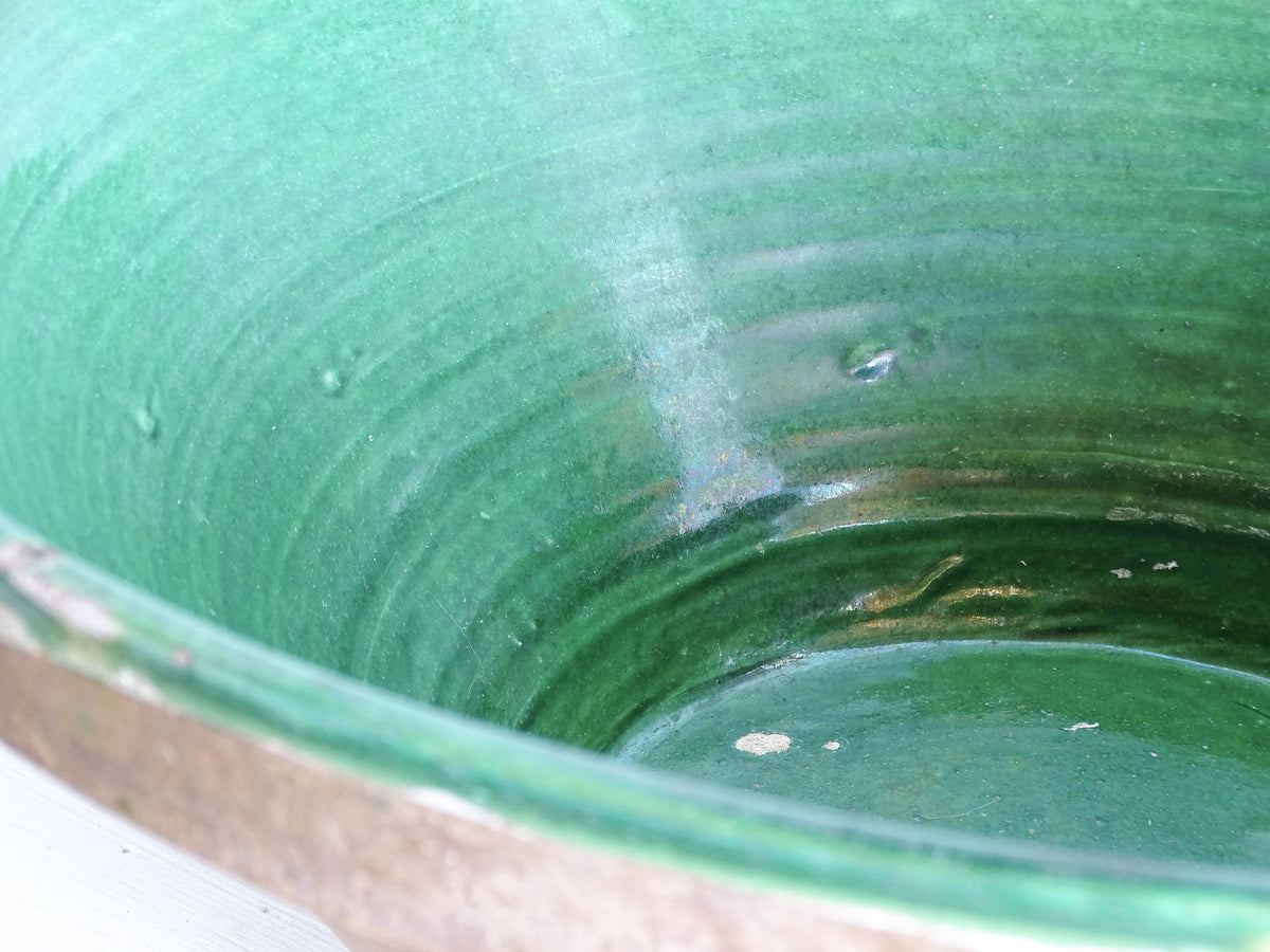 Close-up of the handmade throwing marks and natural glaze variations inside a French antique green pottery bowl.