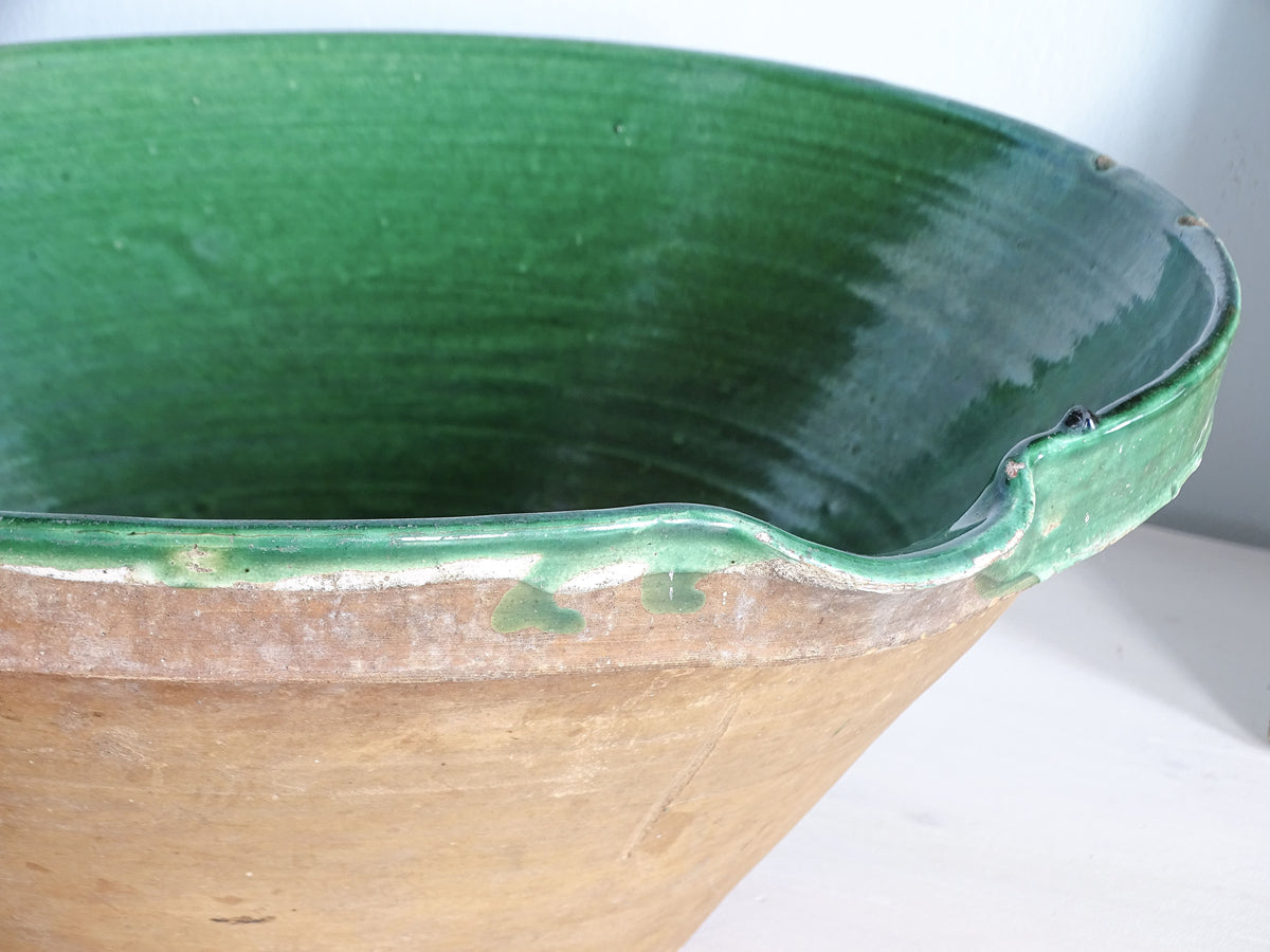 Detail of the pouring lip and green glaze drips on the terracotta exterior of an antique French tian bowl.