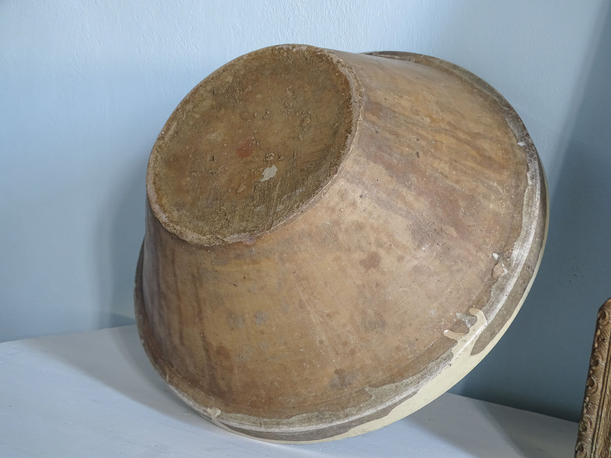Underside detail of a large antique French tian bowl showing the unglazed terracotta exterior, circular foot and traces of pale yellow glaze.