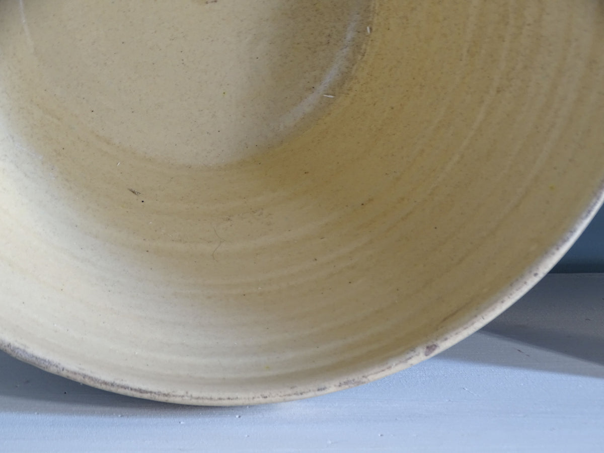 Close-up of the pale yellow glazed interior of an antique French pottery bowl, showing subtle glaze variations and concentric throwing marks.