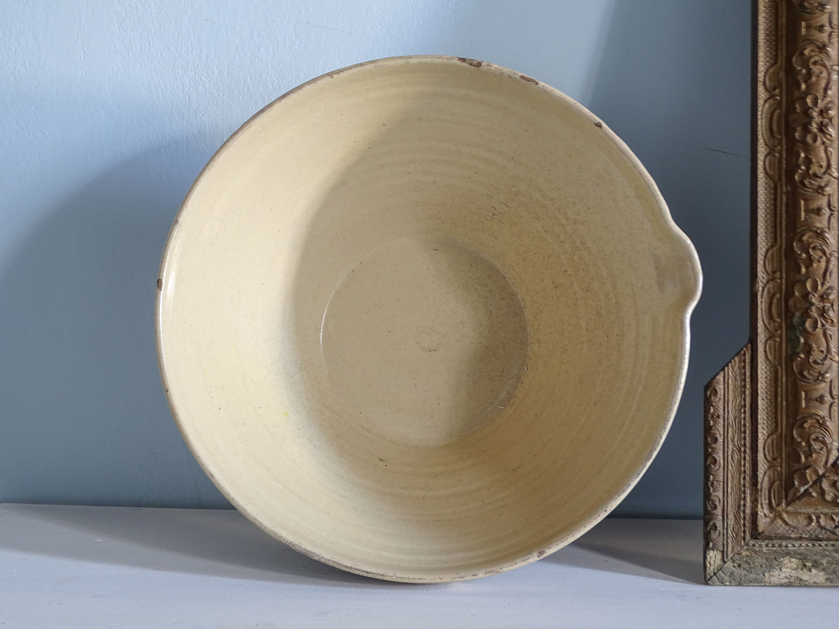 Overhead view of a large antique French tian bowl showing its pale yellow glazed interior, circular base and small pouring spout.