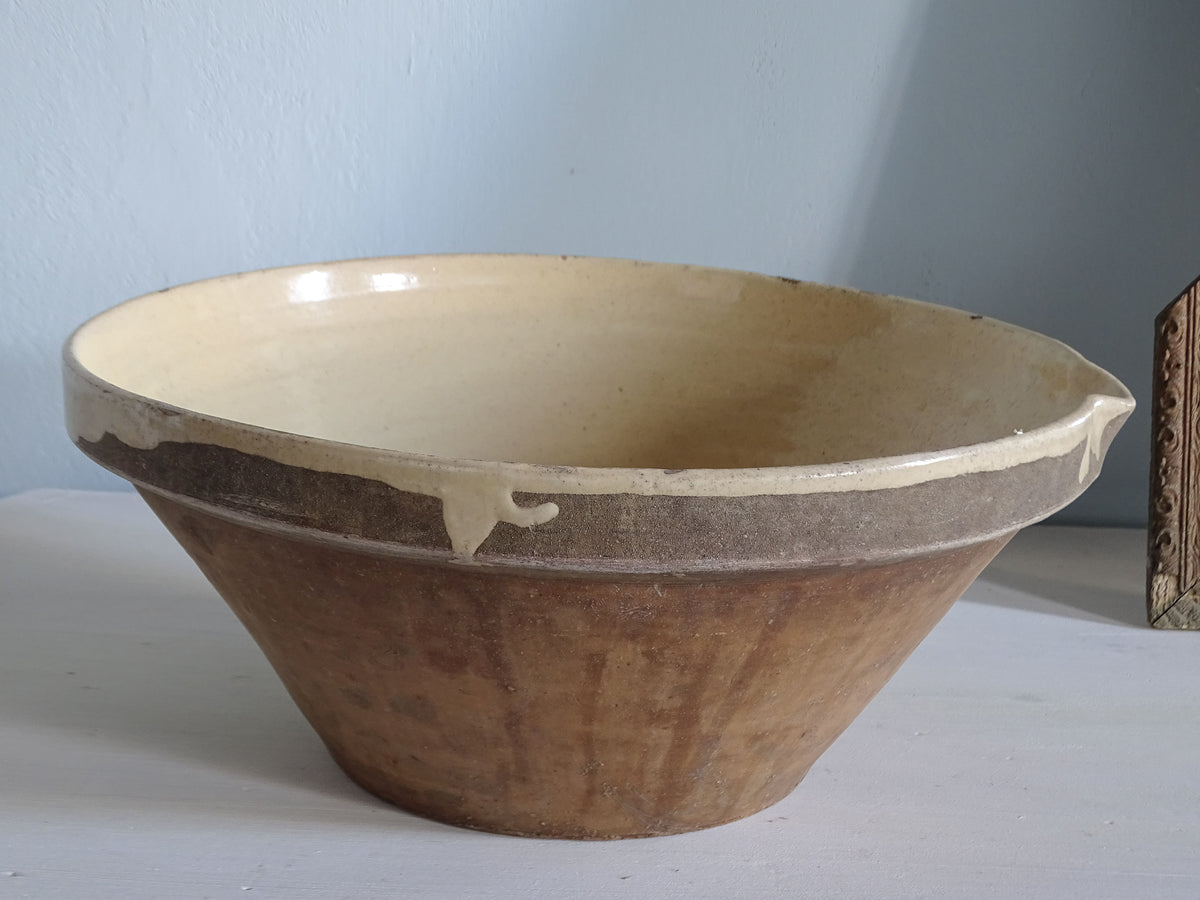 Large French antique tian bowl with pale yellow glazed interior, unglazed terracotta exterior and small pouring spout, viewed from the side.