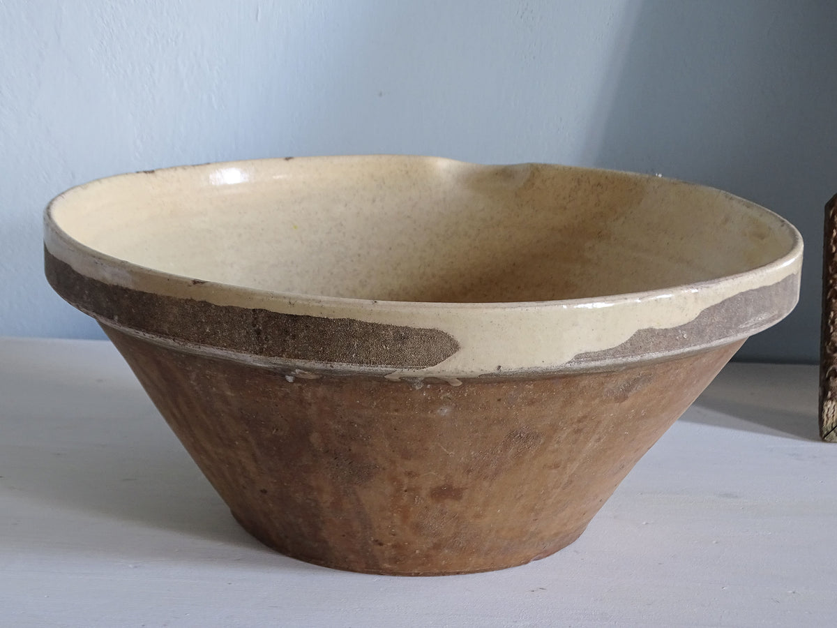 Side view of an antique French grésale bowl showing its wide tapered terracotta form and irregular pale yellow glaze drips around the rim.