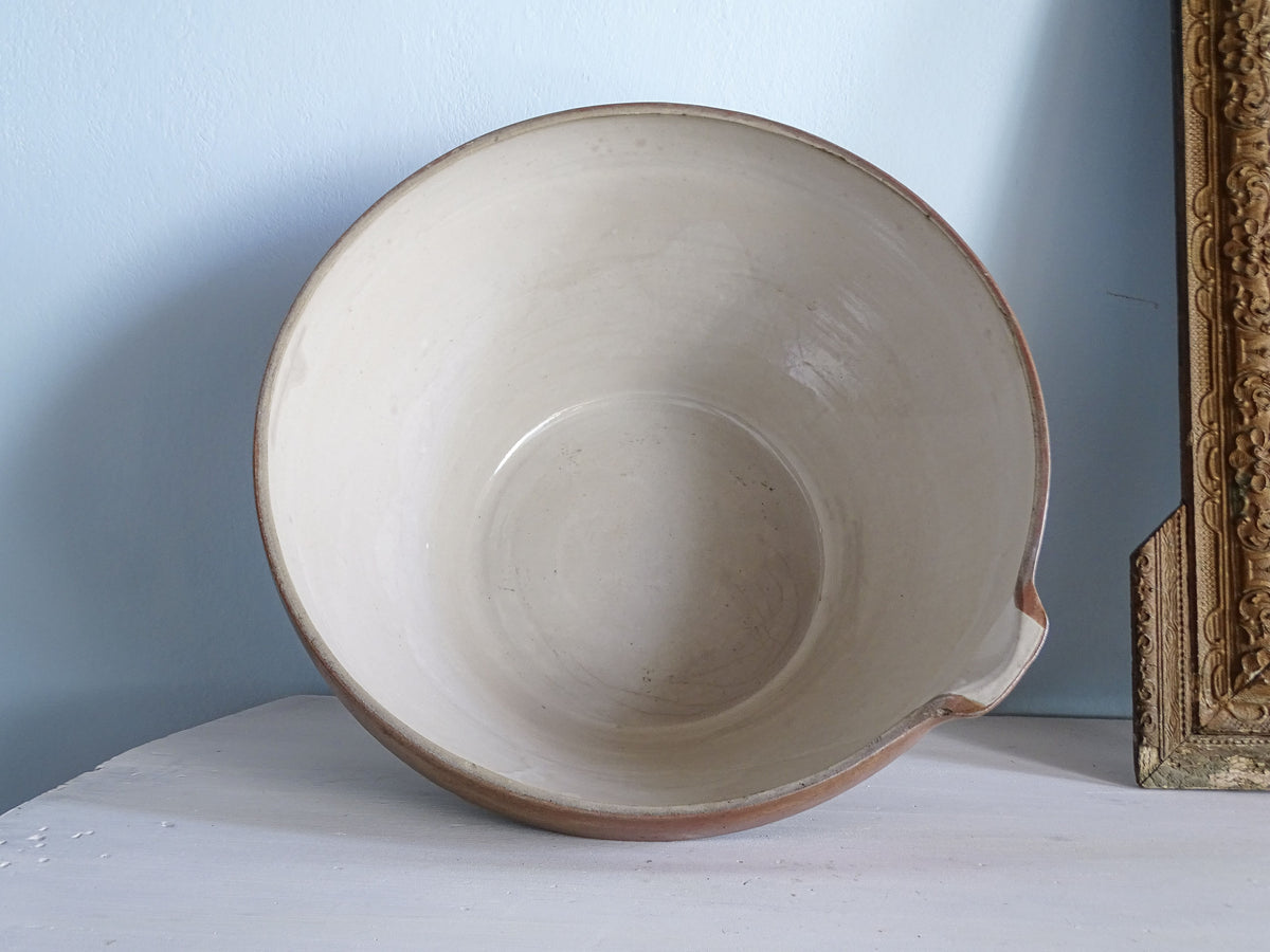 Interior of a large French antique mixing bowl showing its pale cream glaze, rounded base and small pouring spout.